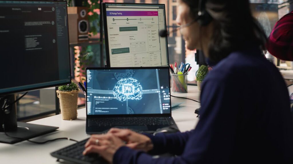 A software developer wearing a headset working at a desk with multiple monitors displaying code and a package tracking dashboard.